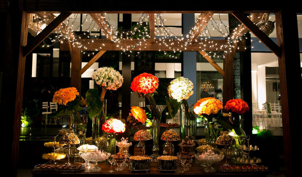 Mesa de doces sob o pergolado de madeira com luzes