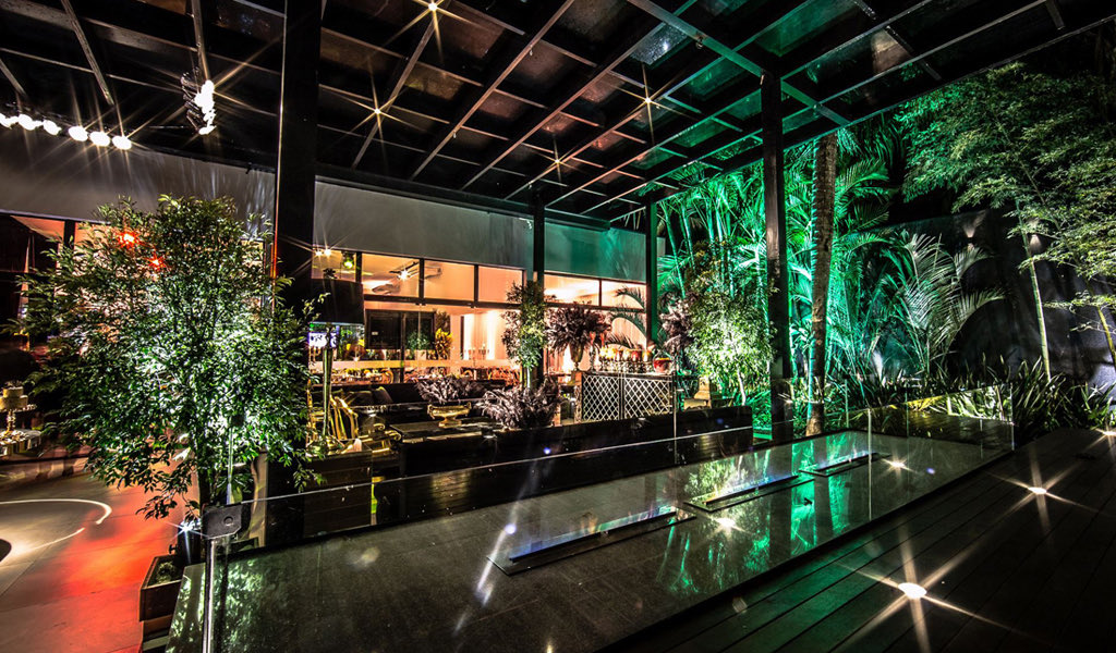 Lounge externo coberto, com espelho d'água e bambus sob luz verde