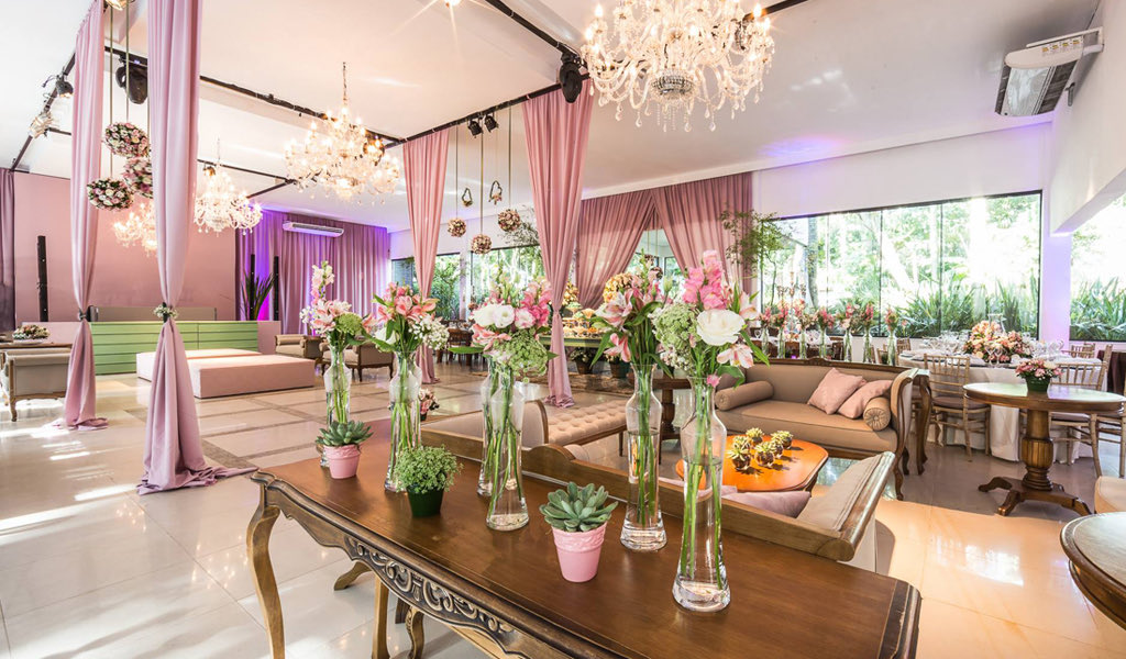 Salão em tons de rosa, com lustres de cristal e cortinas claras